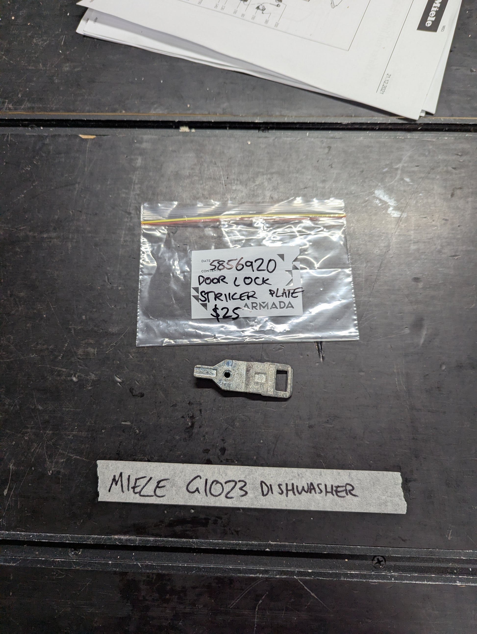 Miele G1023 dishwasher door lock striker plate with labeled packaging on a table