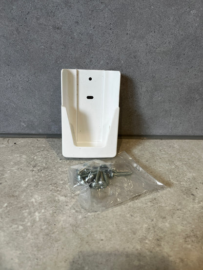 White plastic wall mount bracket with a bag of screws on a gray stone surface