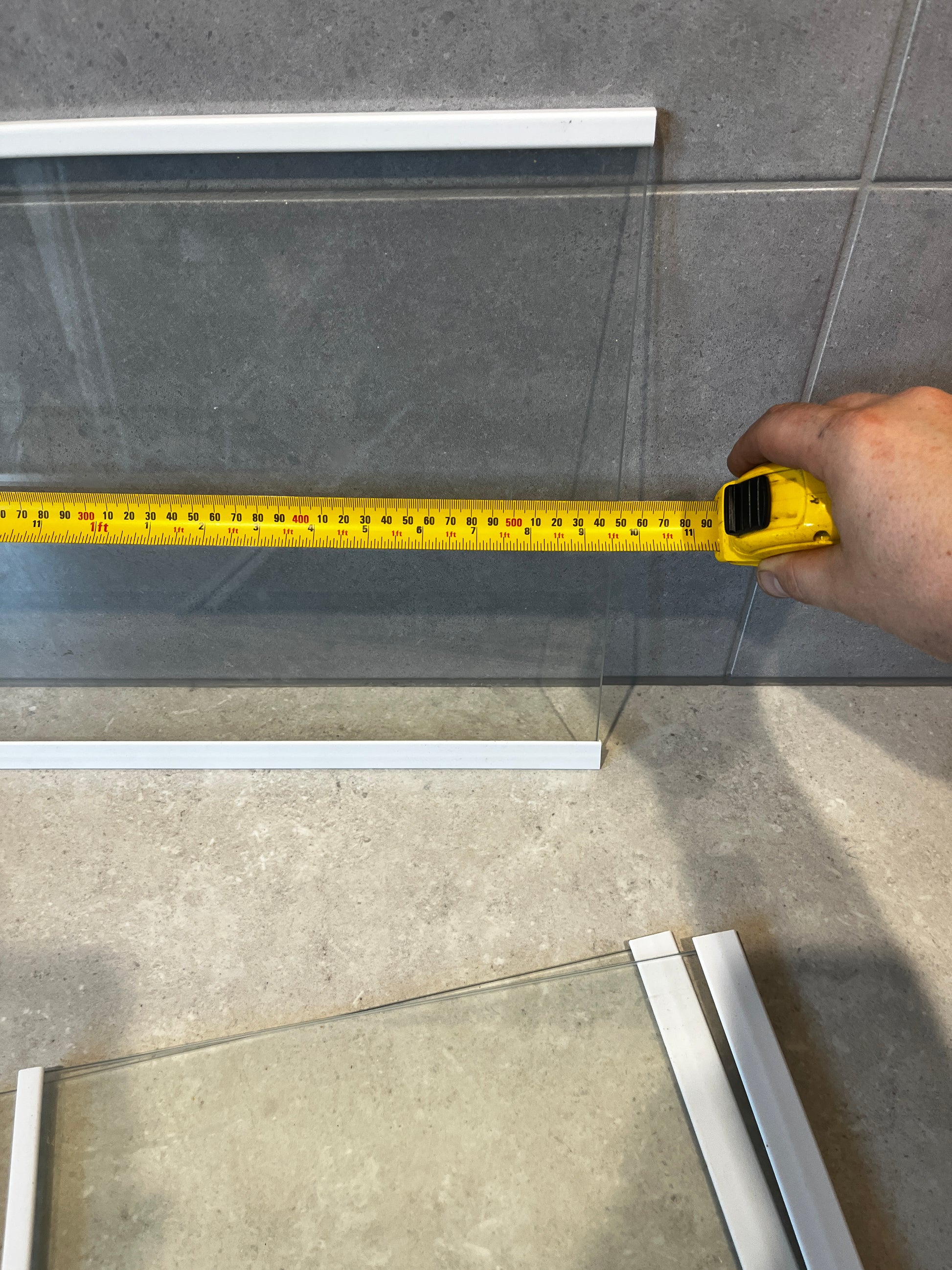 Close-up of clear glass panel with white frames showing a yellow measuring tape indicating length