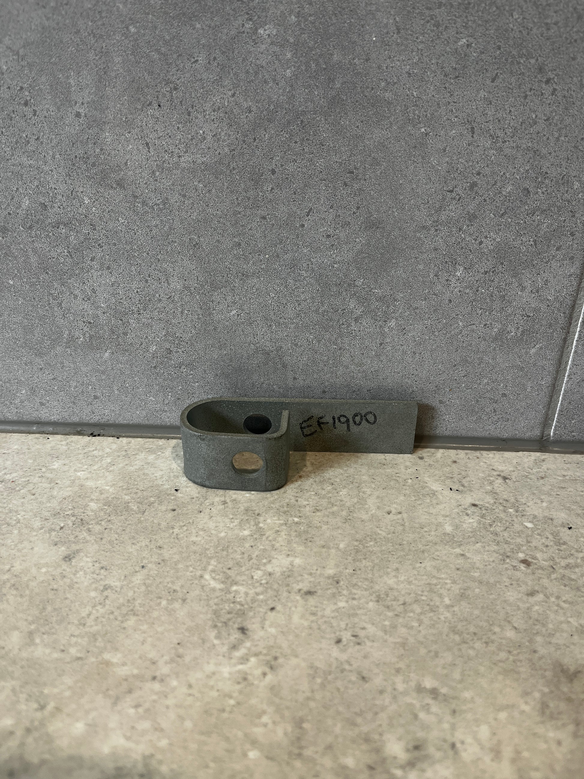 Steel mounting bracket with pre-drilled hole lying flat on a gray surface