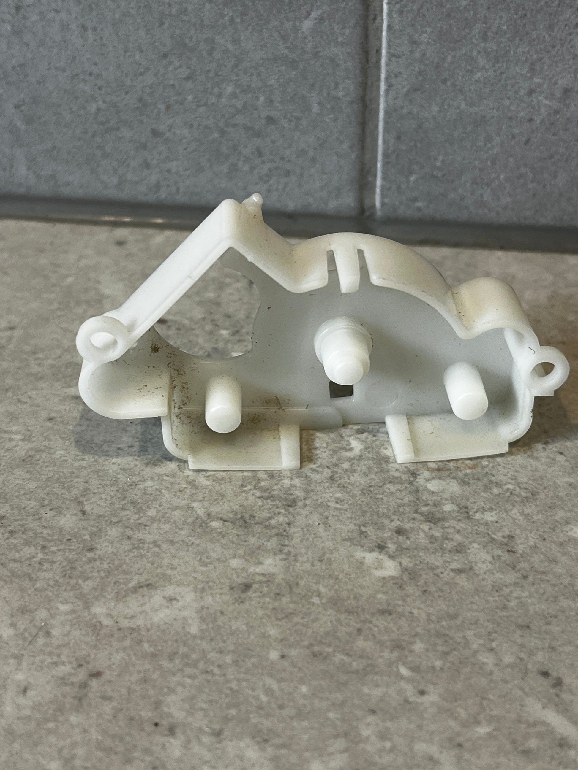 Rear view of white plastic mechanical lever bracket showing attachment pegs