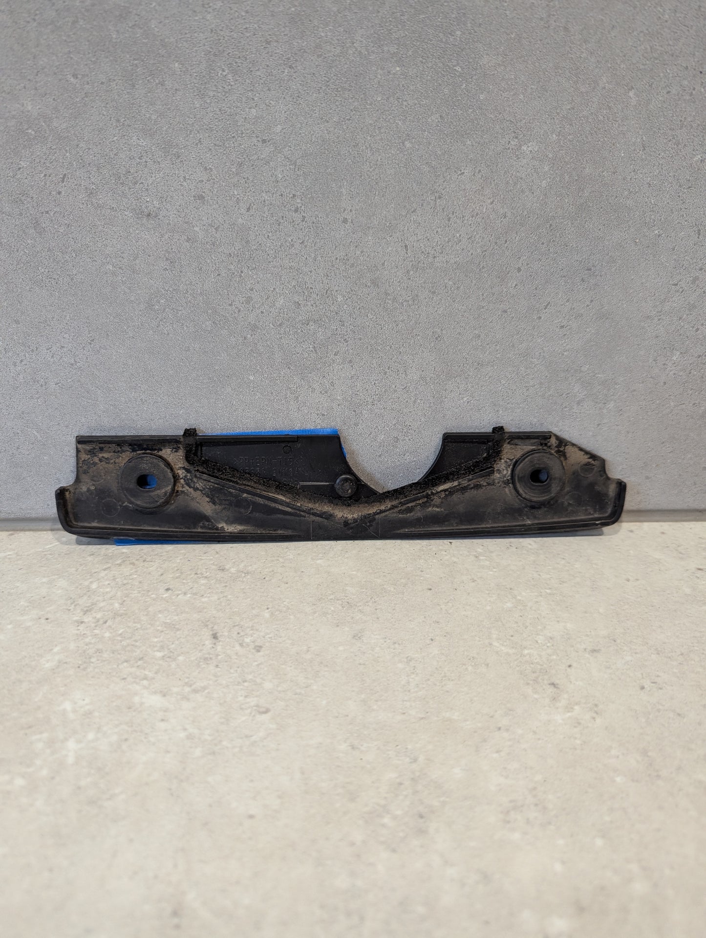 Reverse side of black plastic automotive engine cover bracket showing mounting details