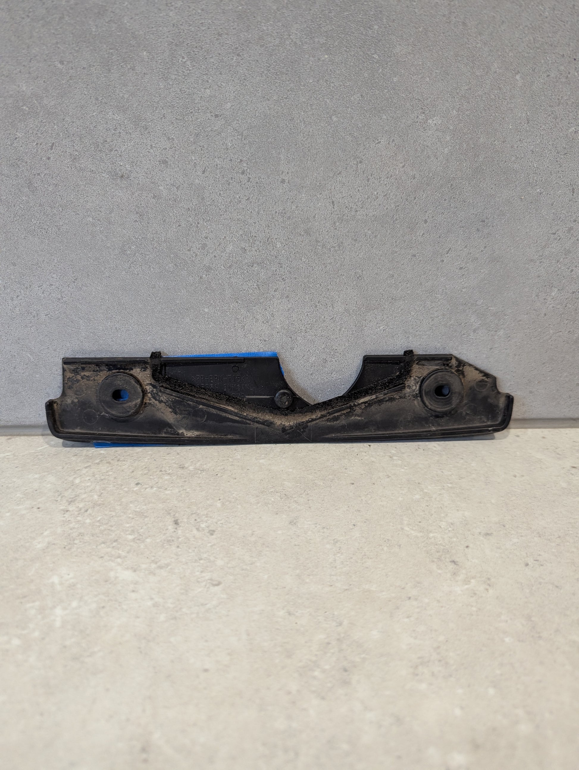 Reverse side of black plastic automotive engine cover bracket showing mounting details
