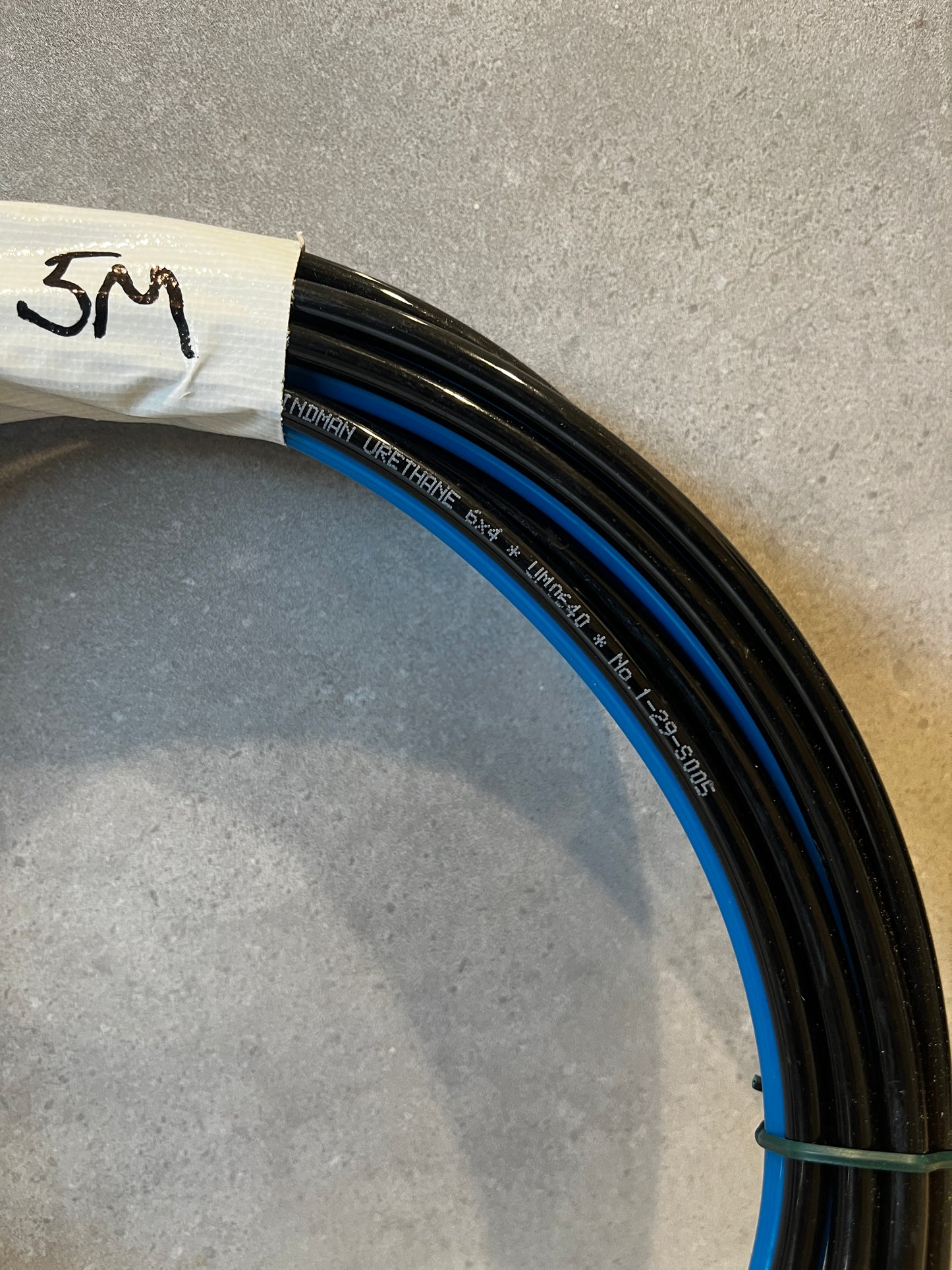 Close-up detail of black urethane air hose tube with blue stripe and label marked 5M
