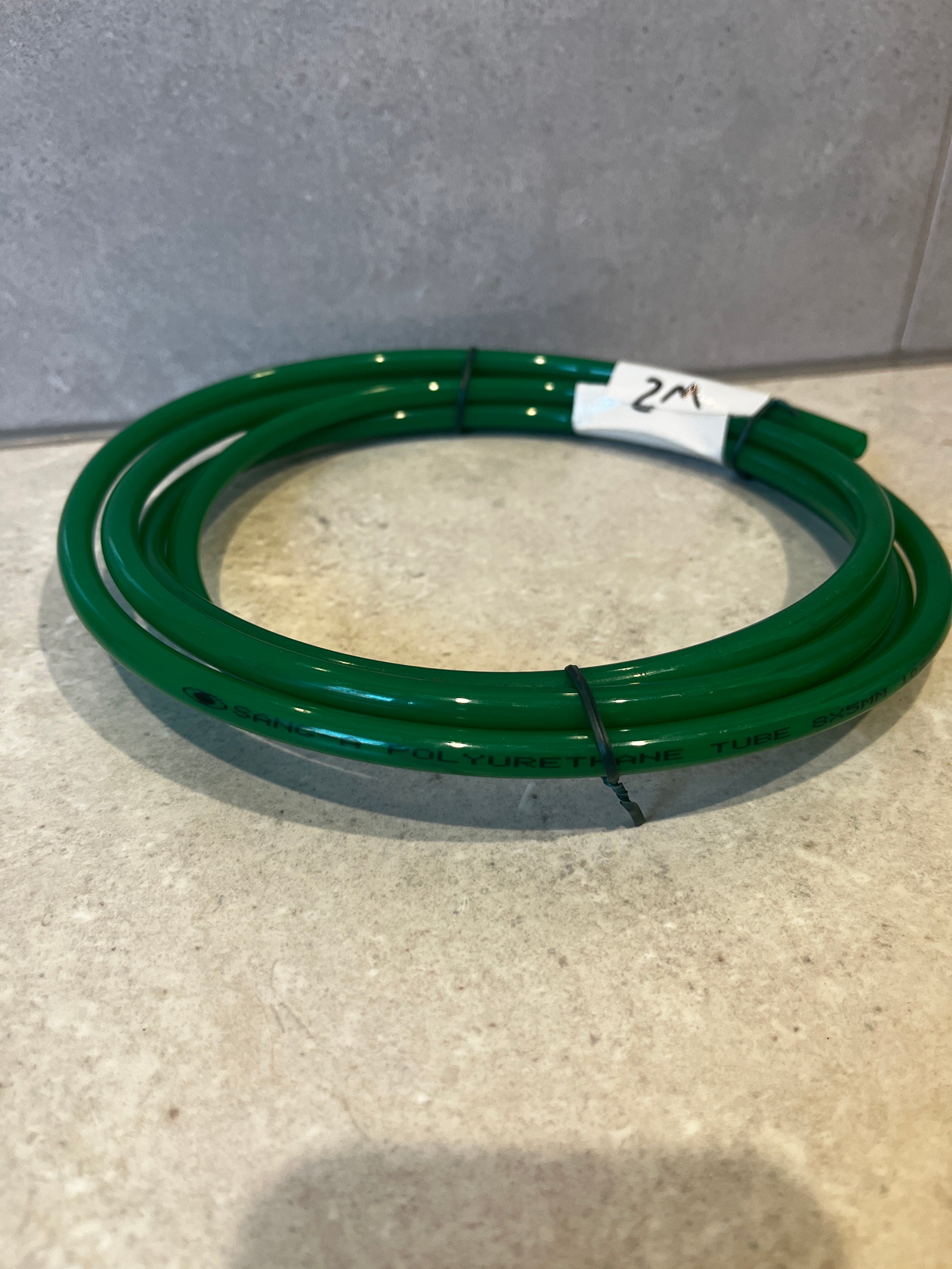 Close-up side view of coiled green polyurethane tube with 2 meter label