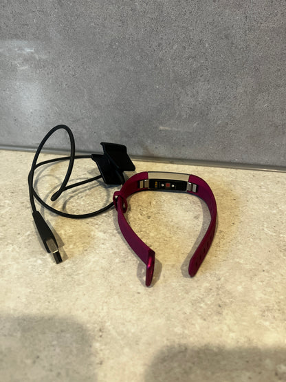 Back view of smart fitness tracker showing sensors with USB charging cable on a stone surface