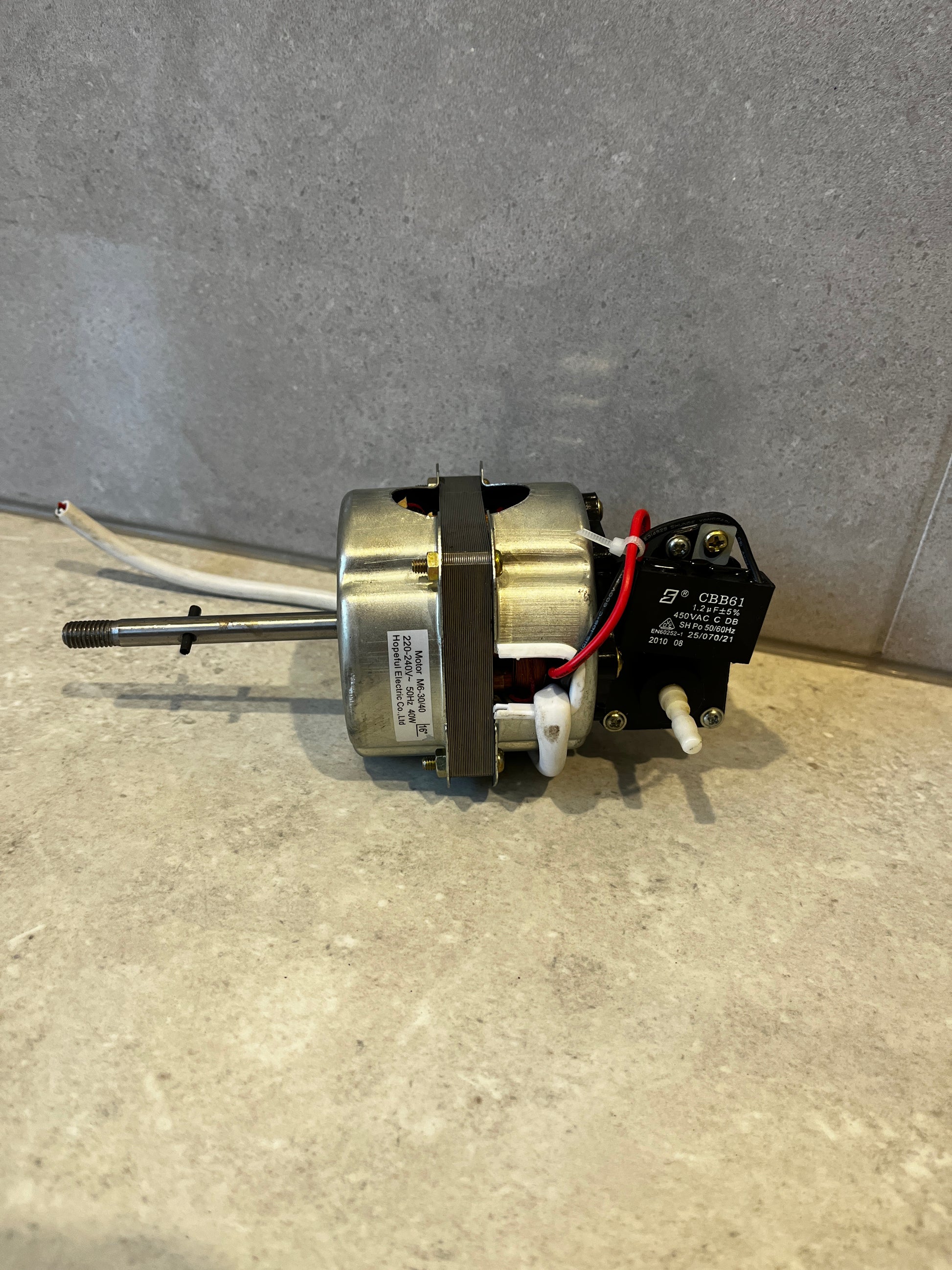 Electric fan motor with wiring and capacitor visible, positioned sideways on surface
