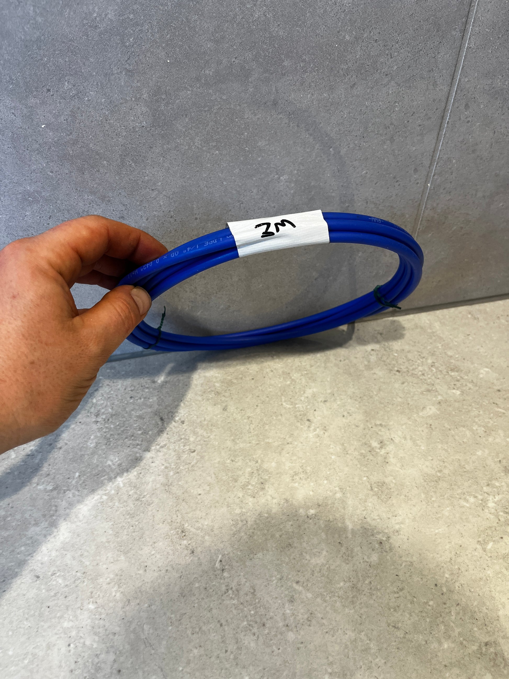 Hand holding a coiled blue electrical cable labeled '2M' against a tiled background