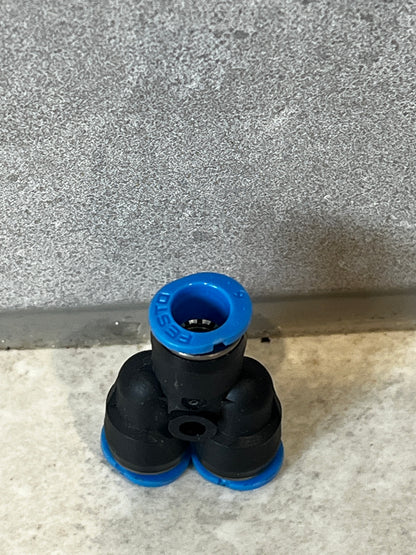 Front angle view of pneumatic Y fitting with blue Festo ring and black polymer structure on gray stone background