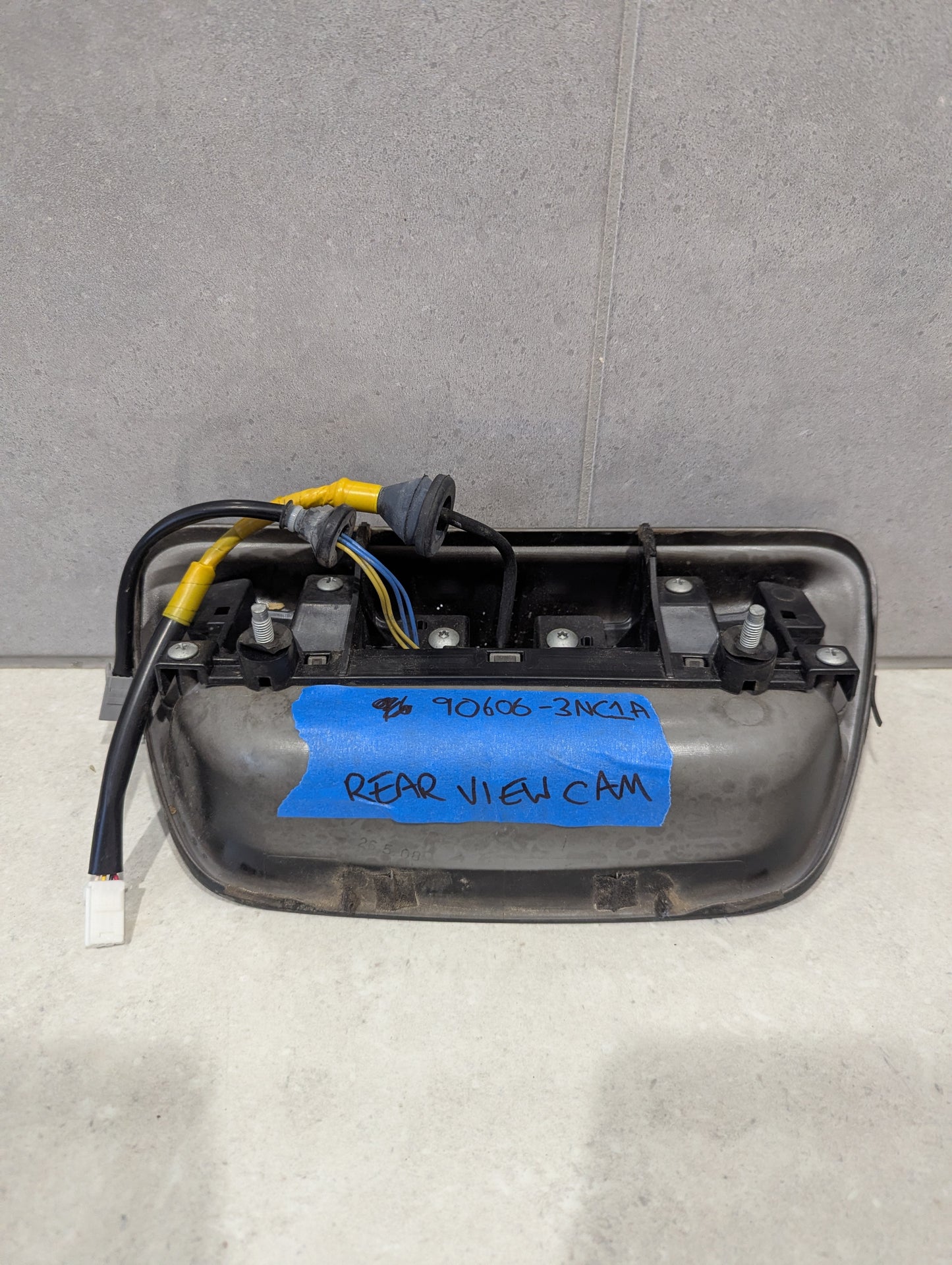 Back view of rear view camera tailgate handle showing wiring, mounting, and label with part number
