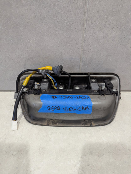 Back view of rear view camera tailgate handle showing wiring, mounting, and label with part number