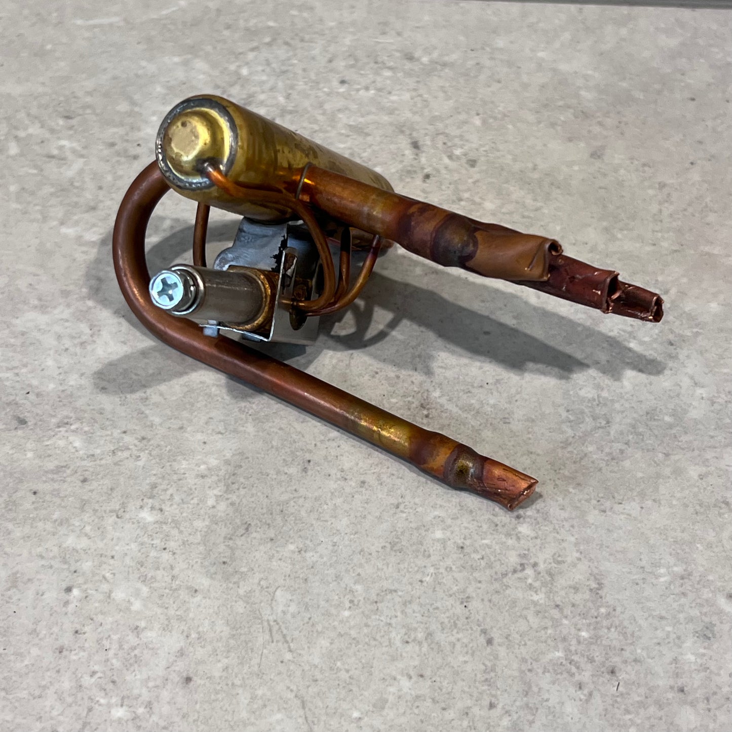 Side angle of copper and brass 4-way reversing valve on a gray surface
