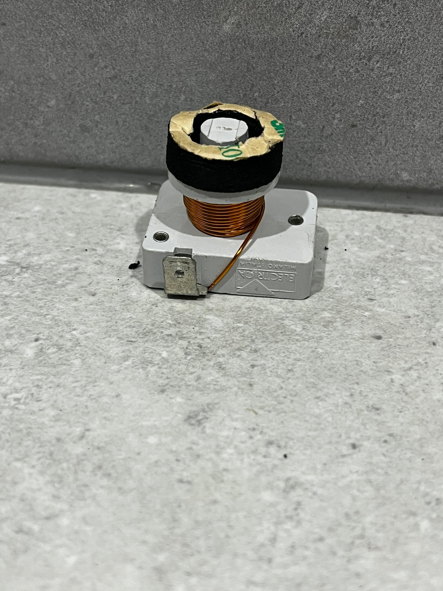 Side view of copper coil component with visible wire winding and plastic base