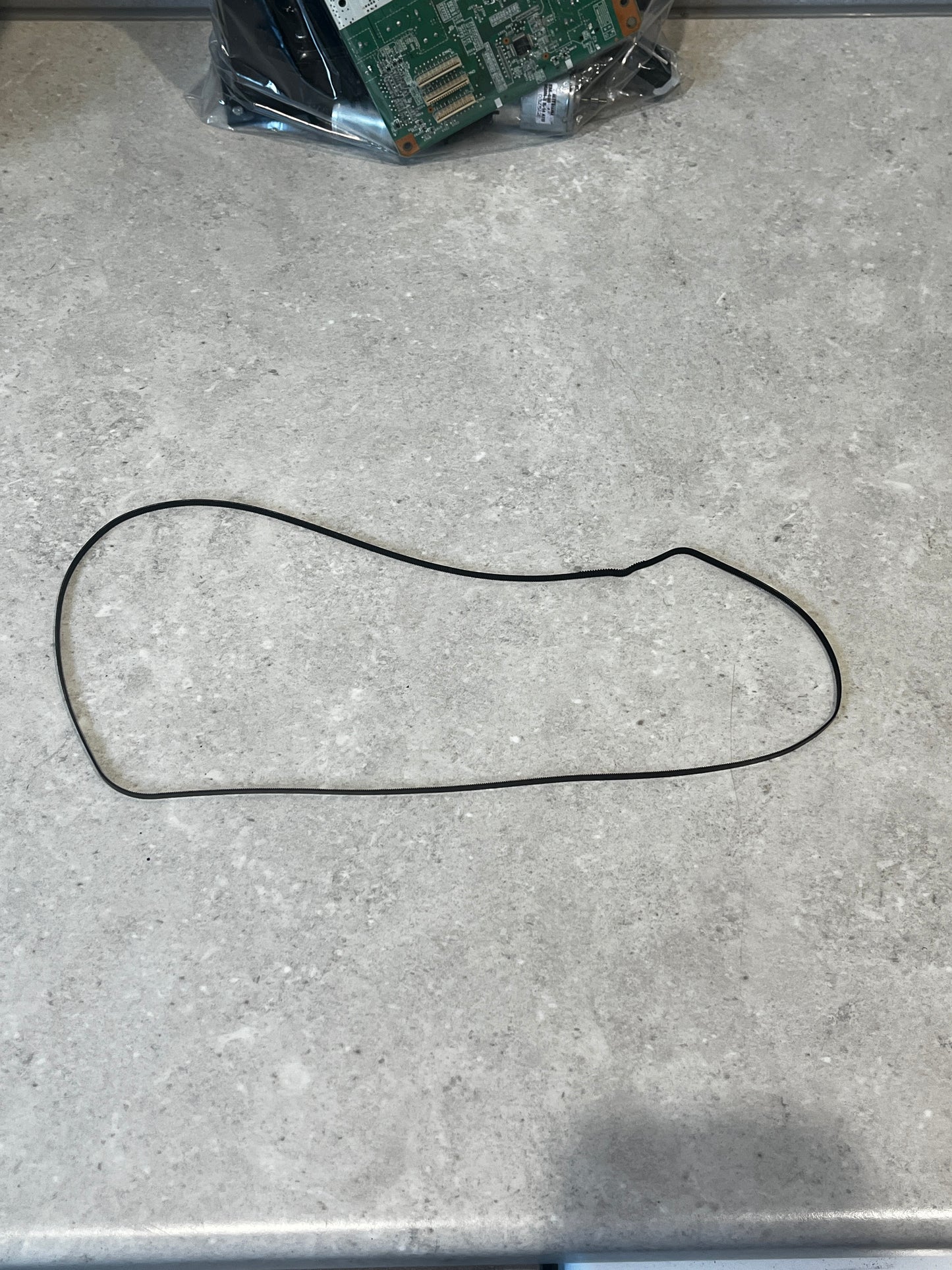 Full view of the flexible rubber timing belt laid out on a countertop with electronic components in the background
