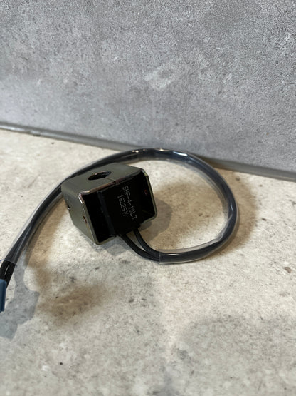 Back view of industrial solenoid coil showing wiring and connector on gray surface