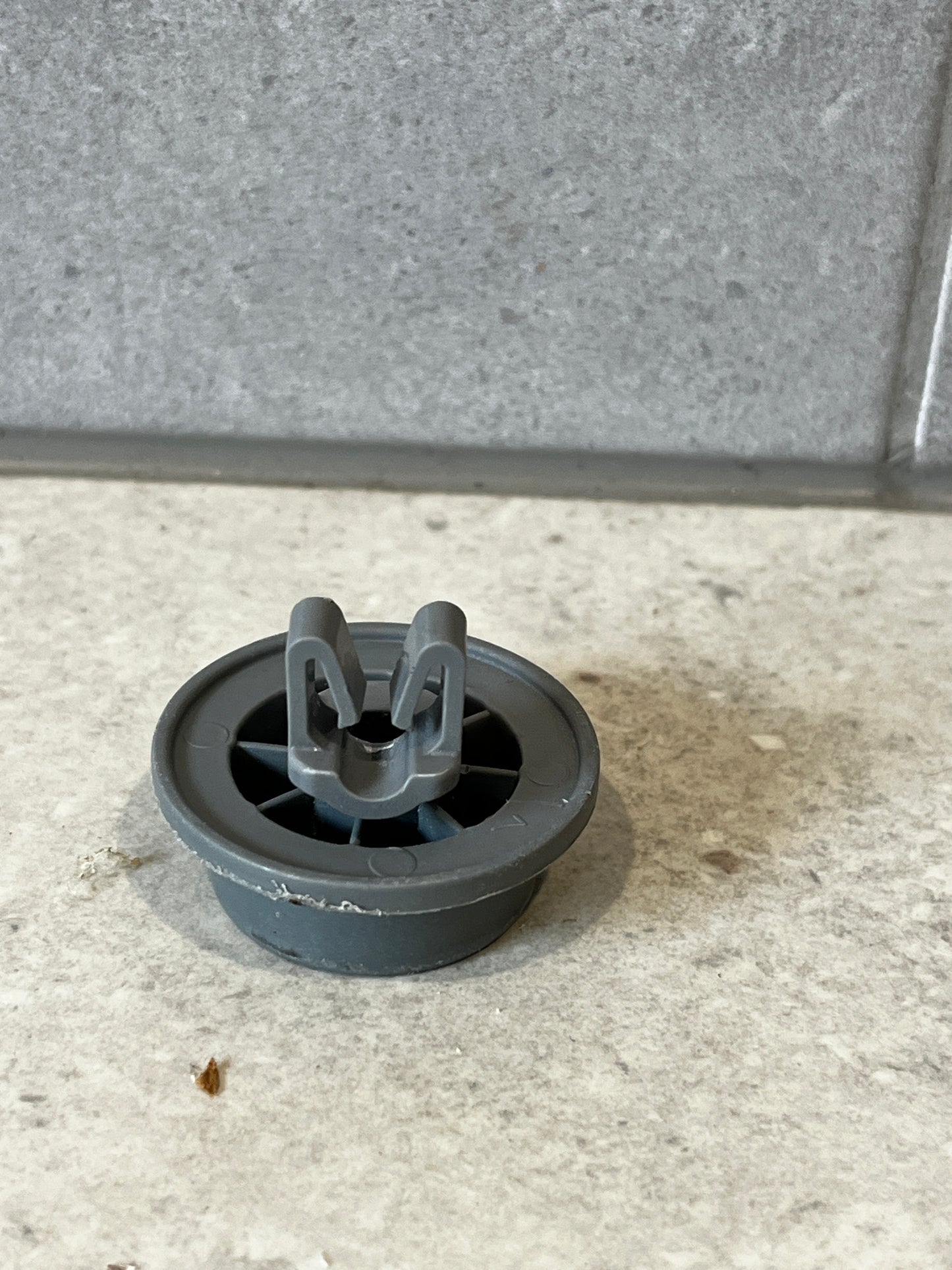Gray plastic dishwasher lower rack wheel viewed from above showing attachment clip and spoke design