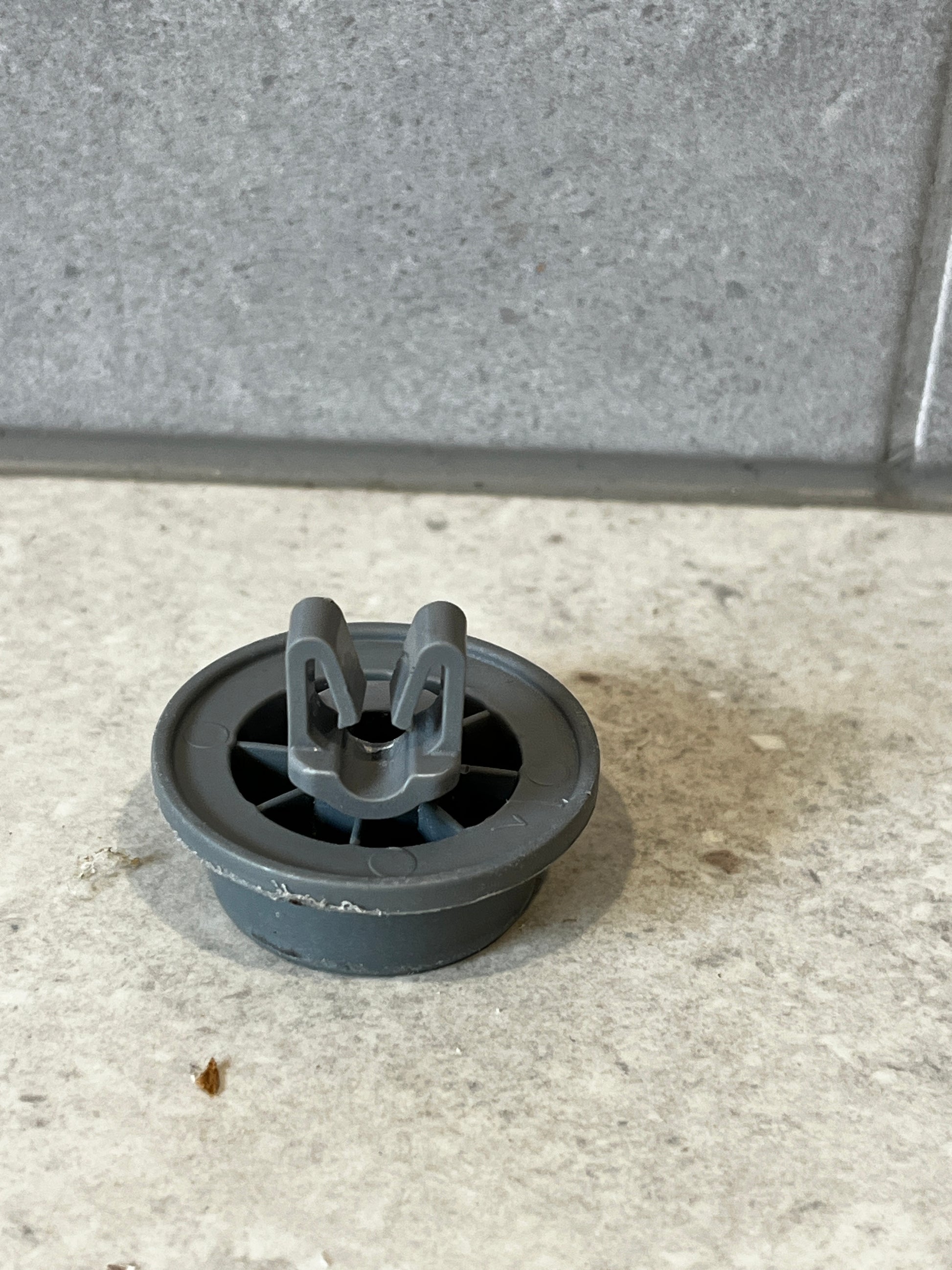 Gray plastic dishwasher lower rack wheel viewed from above showing attachment clip and spoke design