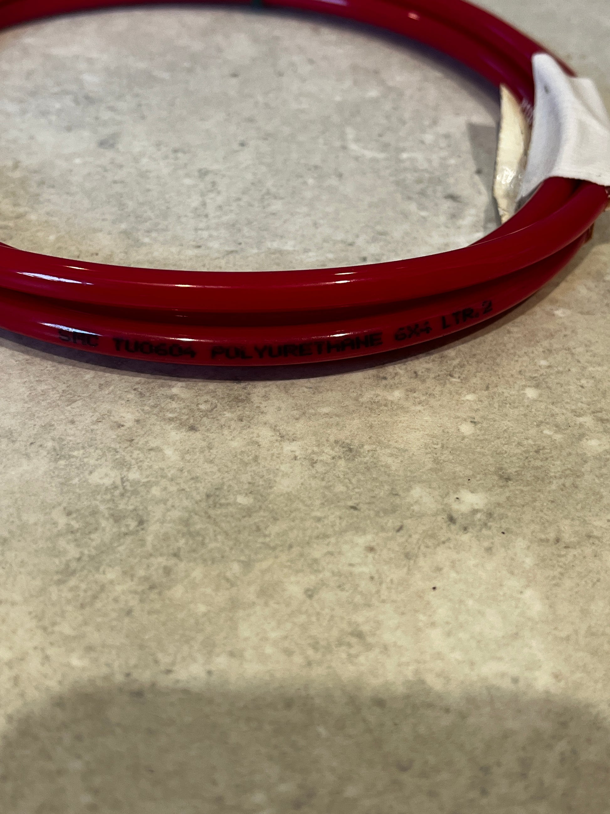 Close-up of red polyurethane tubing with material and size markings on concrete surface