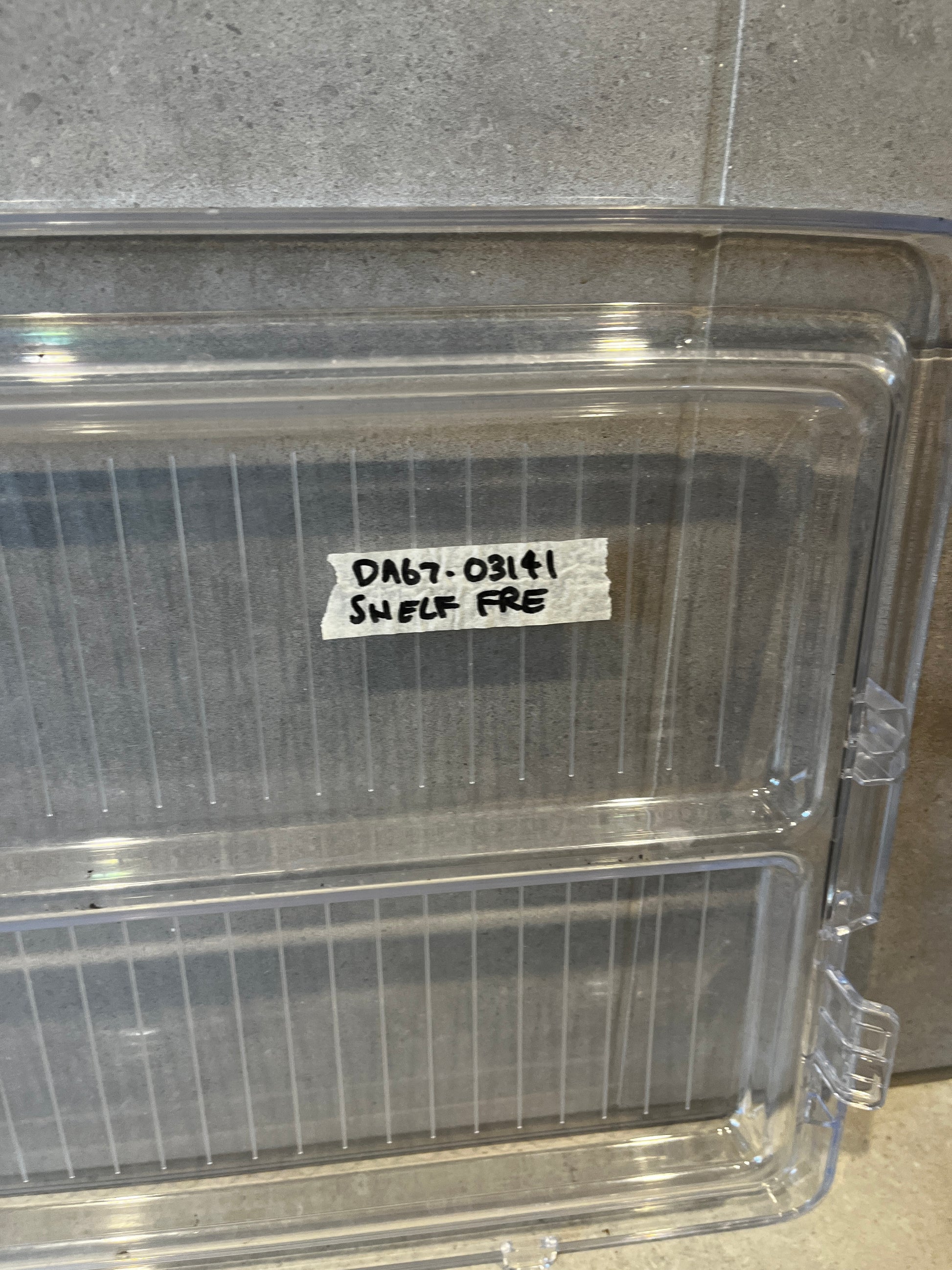 Close-up of label reading 'DA67-03141 SHELF FRF' on transparent refrigerator shelf bin