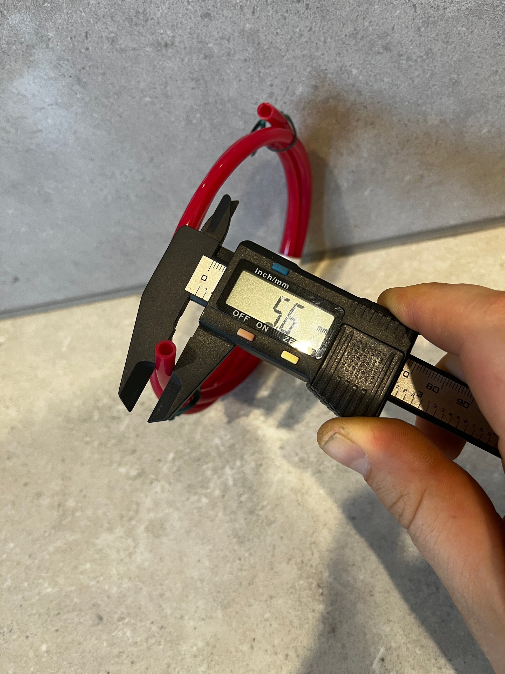 Digital caliper measuring the outer diameter of red flexible tubing at 5.6mm
