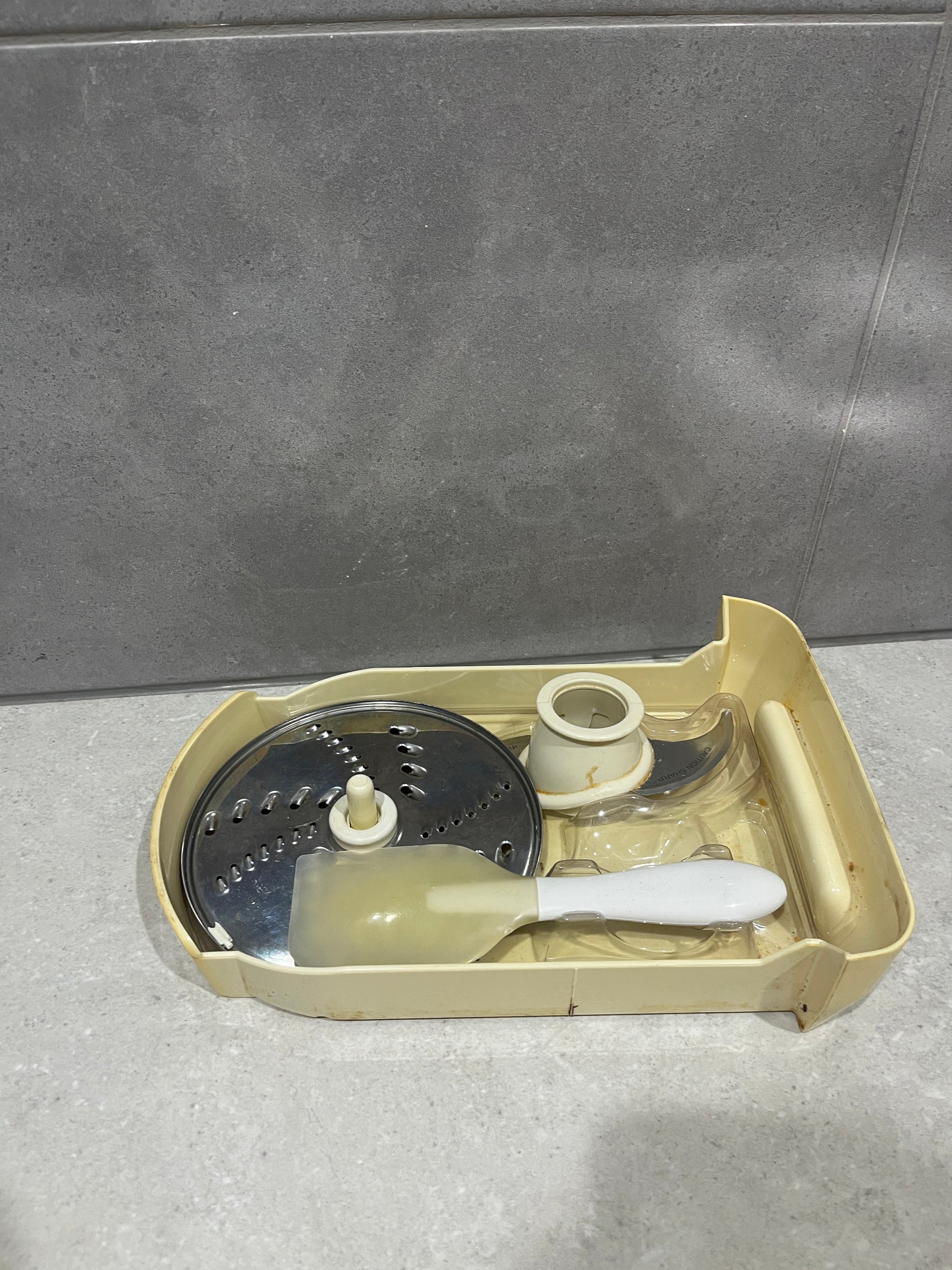 Food processor accessory kit showing stainless steel discs and spatula neatly arranged in storage tray