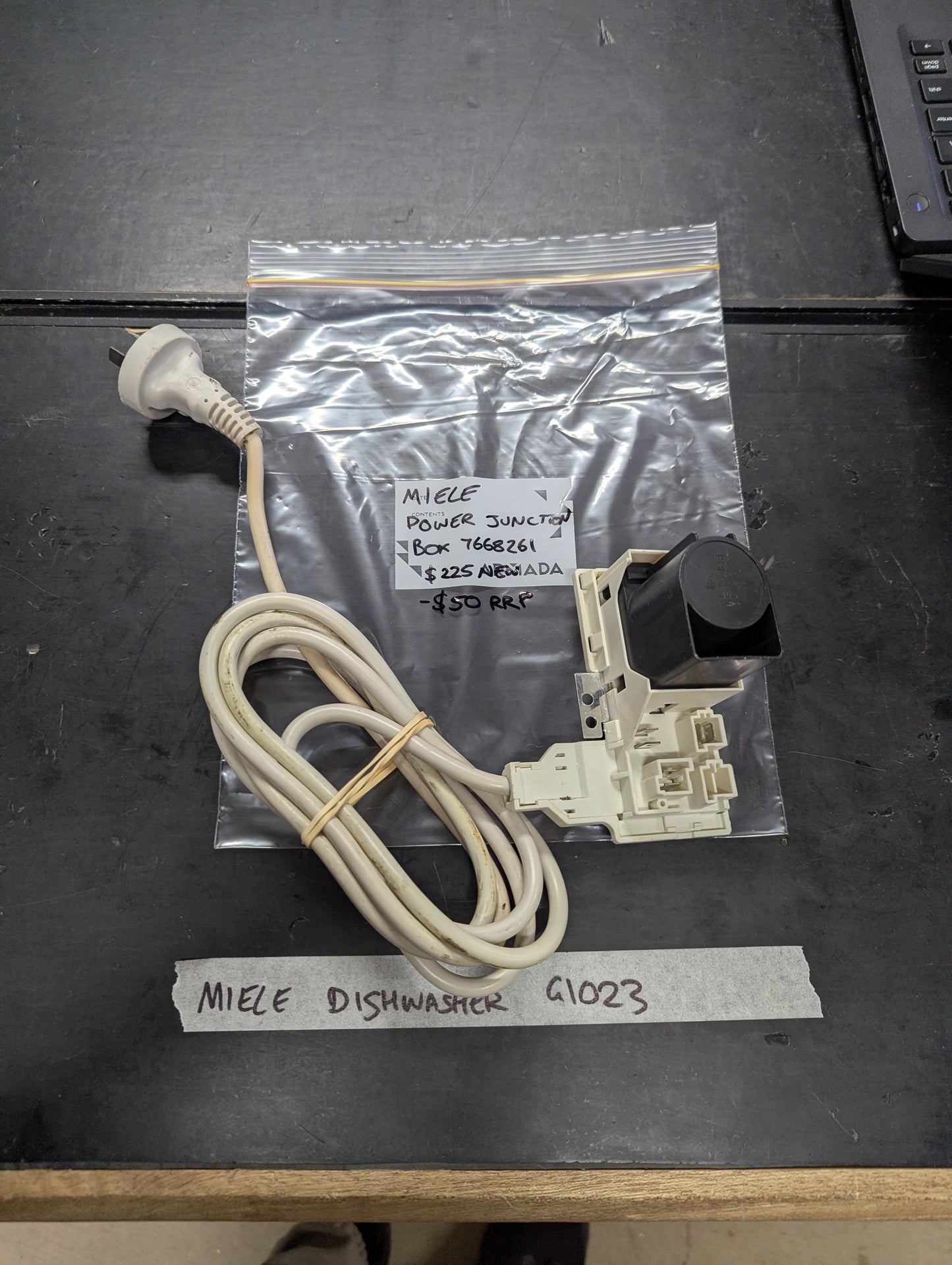 Top view of Miele dishwasher G1023 power junction box and cord next to labeled bag