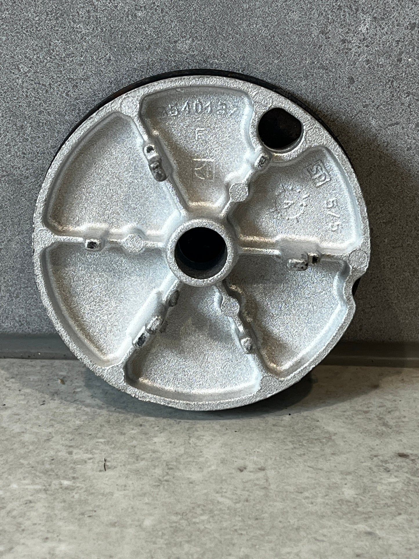 Bottom view of a round cast metal end cap showing structural details and technical markings