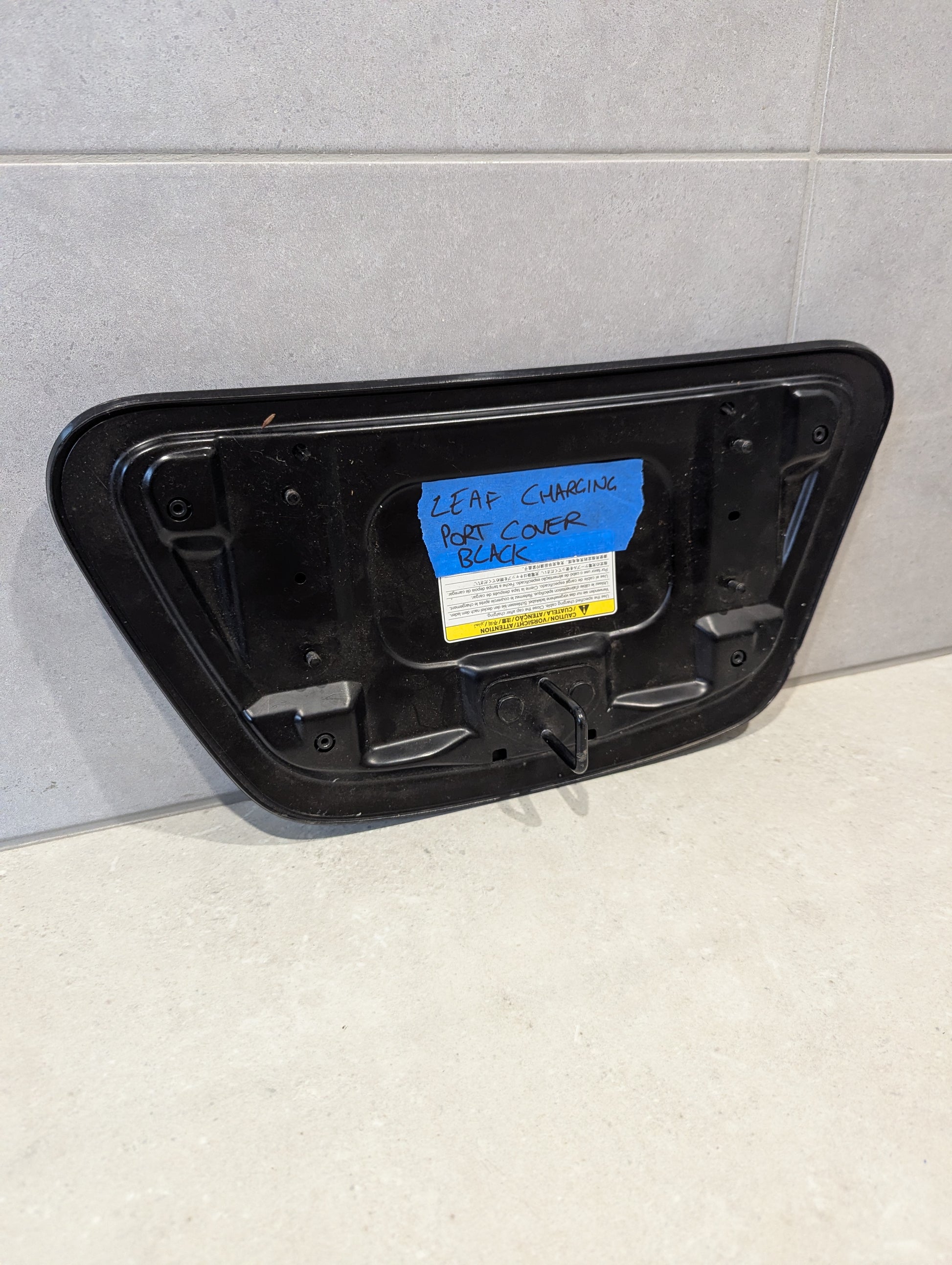 Rear view of Nissan Leaf charging port cover showing mounting points and label