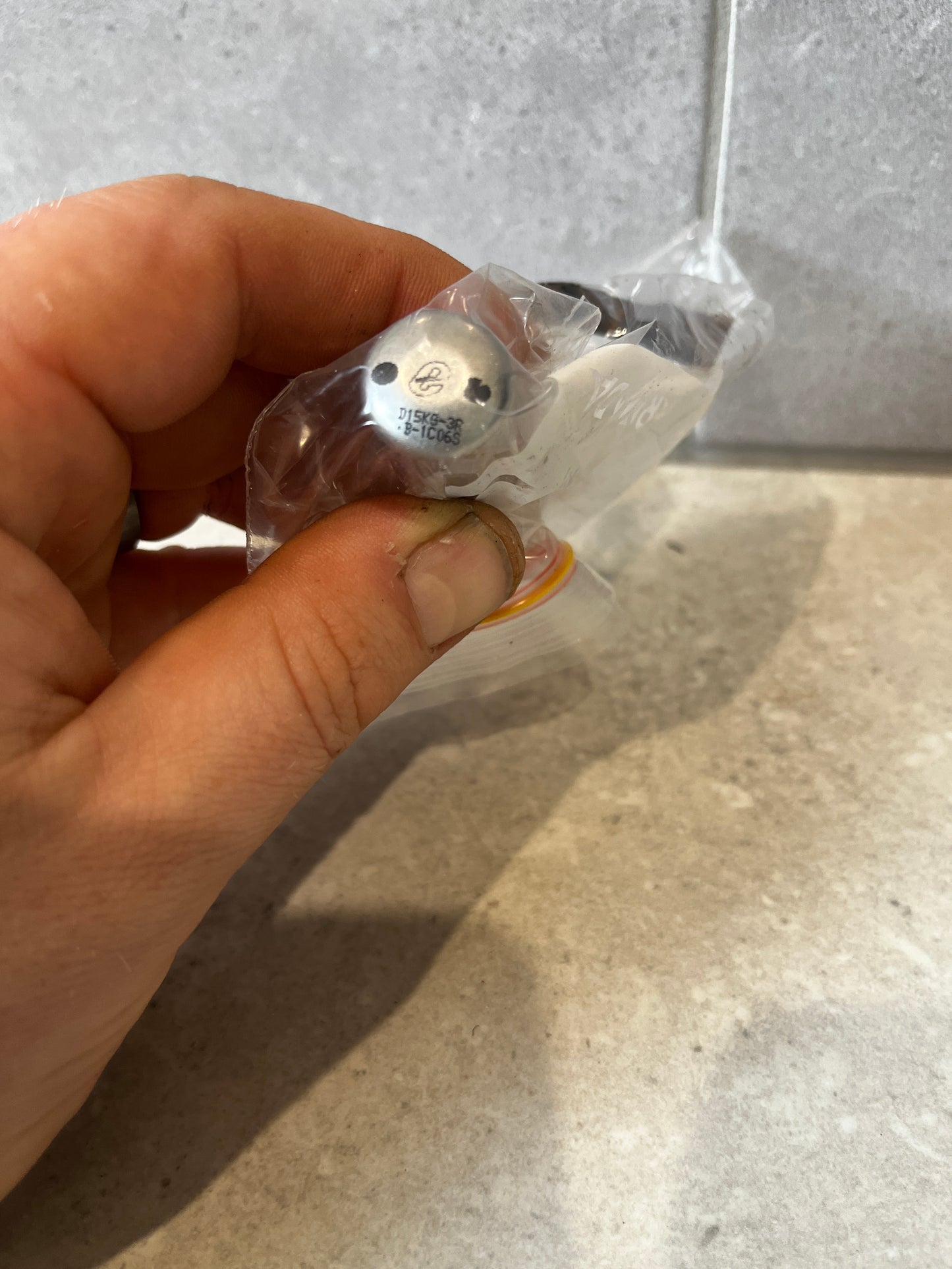 Close-up view of metal nozzle fitting with visible engravings in a plastic bag