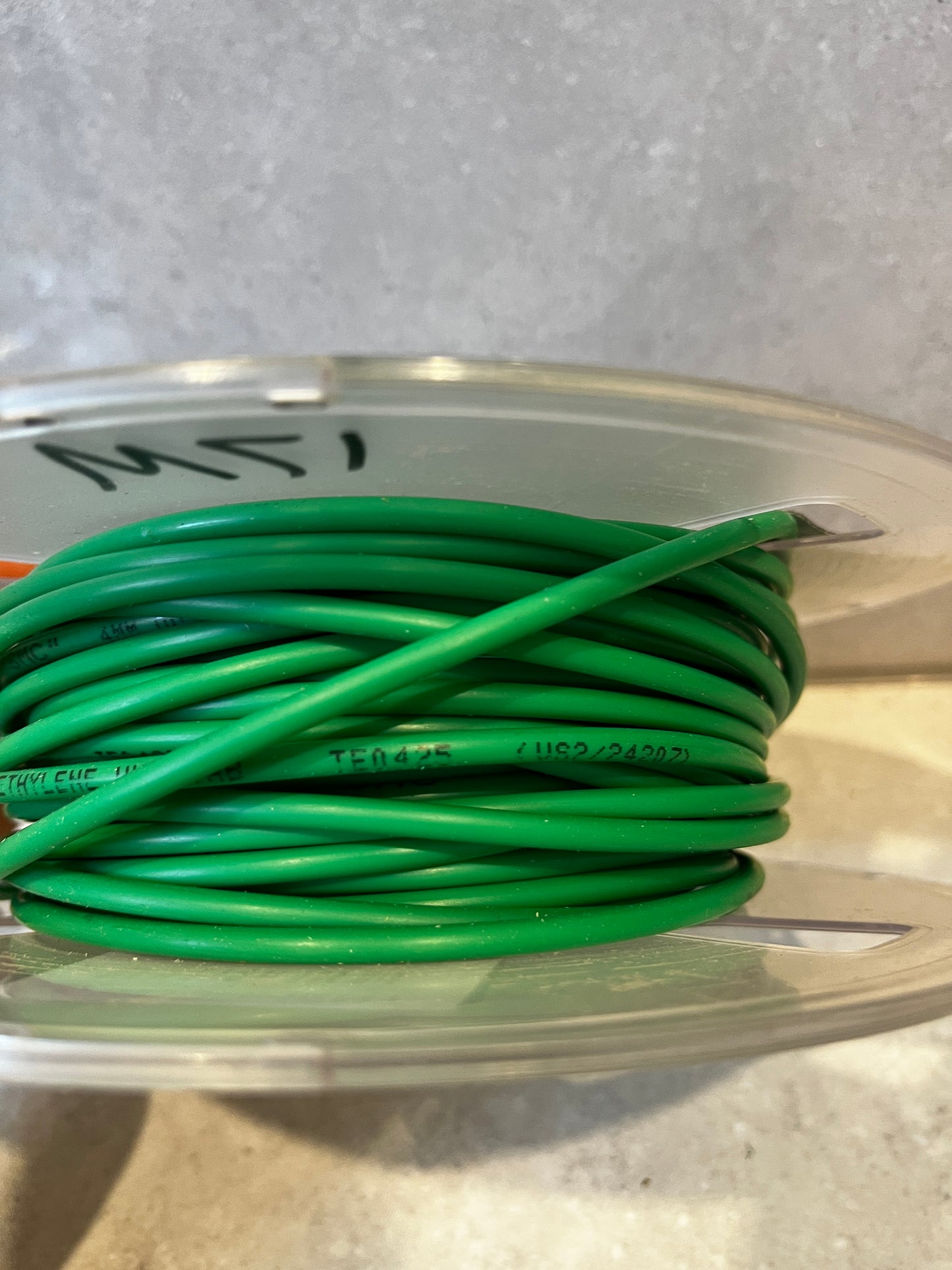 Side view of green insulated electrical wire wrapped around clear plastic spool