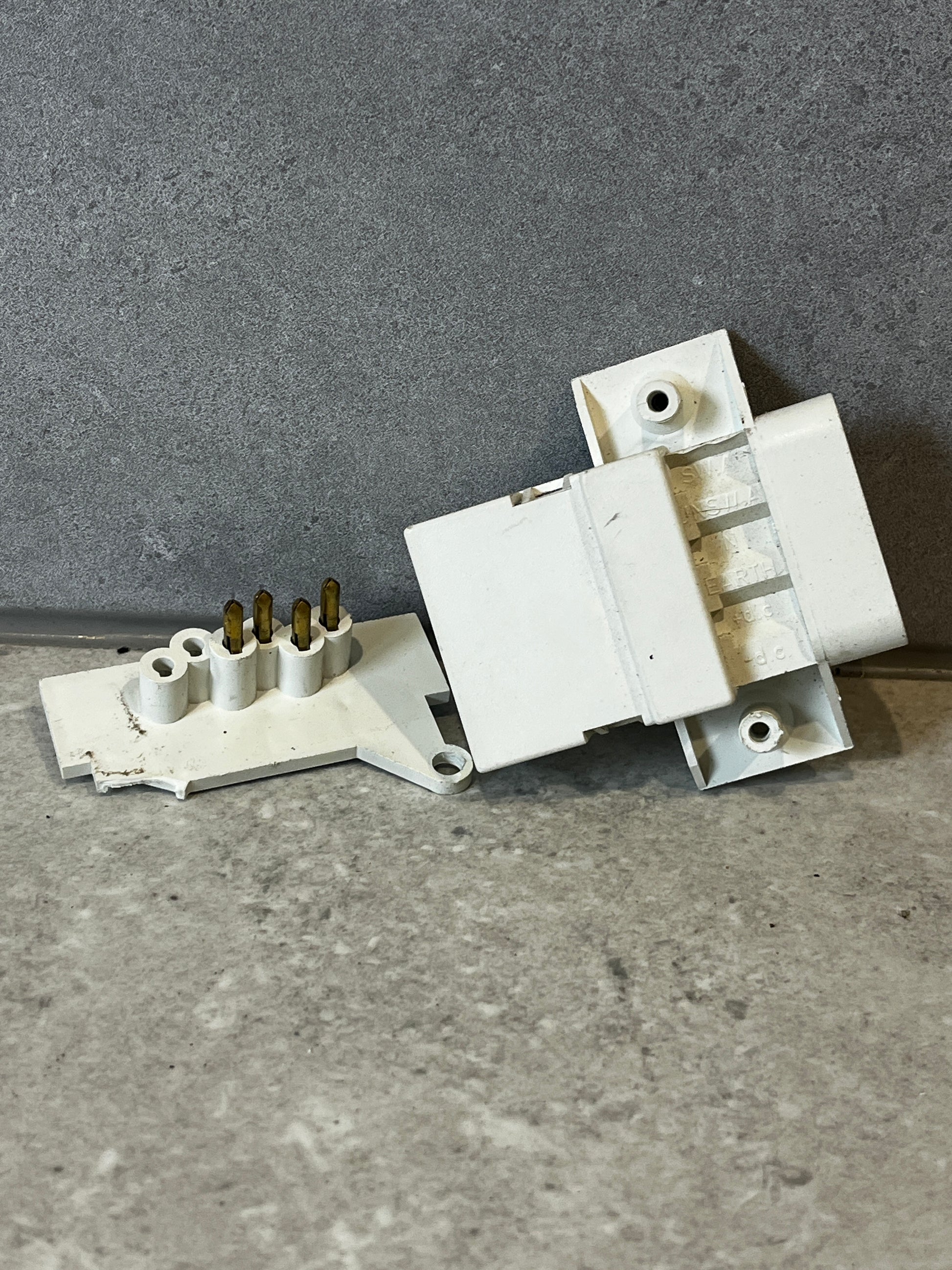 Angled view of white multi-pin electrical connector highlighting connection pins and mounting points