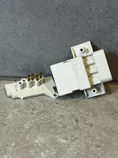 Angled view of white multi-pin electrical connector highlighting connection pins and mounting points