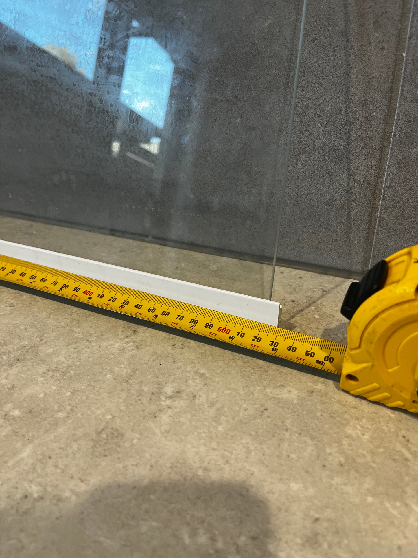 Close-up of clear safety glass panel with measuring tape showing width