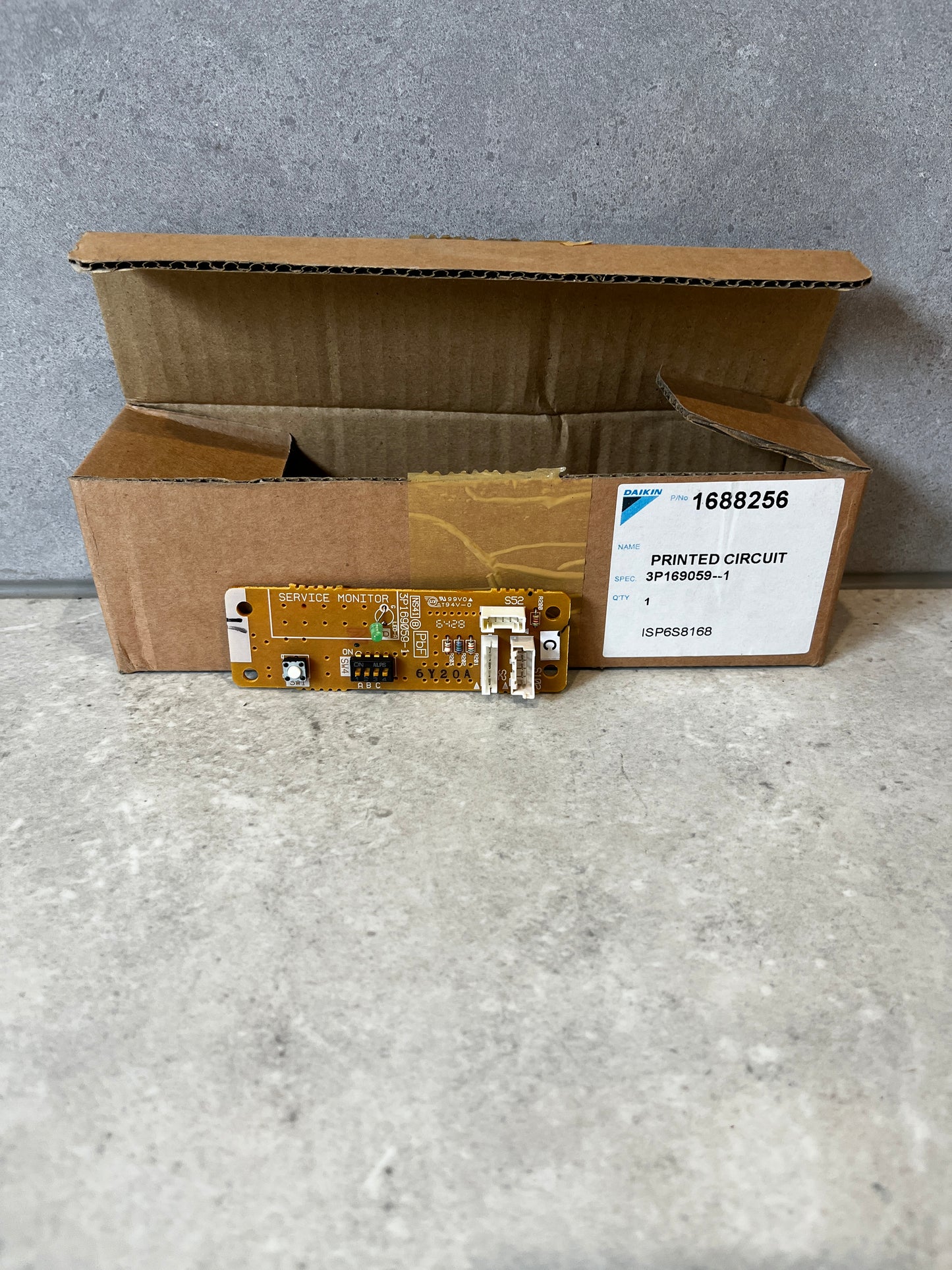 Daikin printed circuit board in front of open shipping box on gray surface