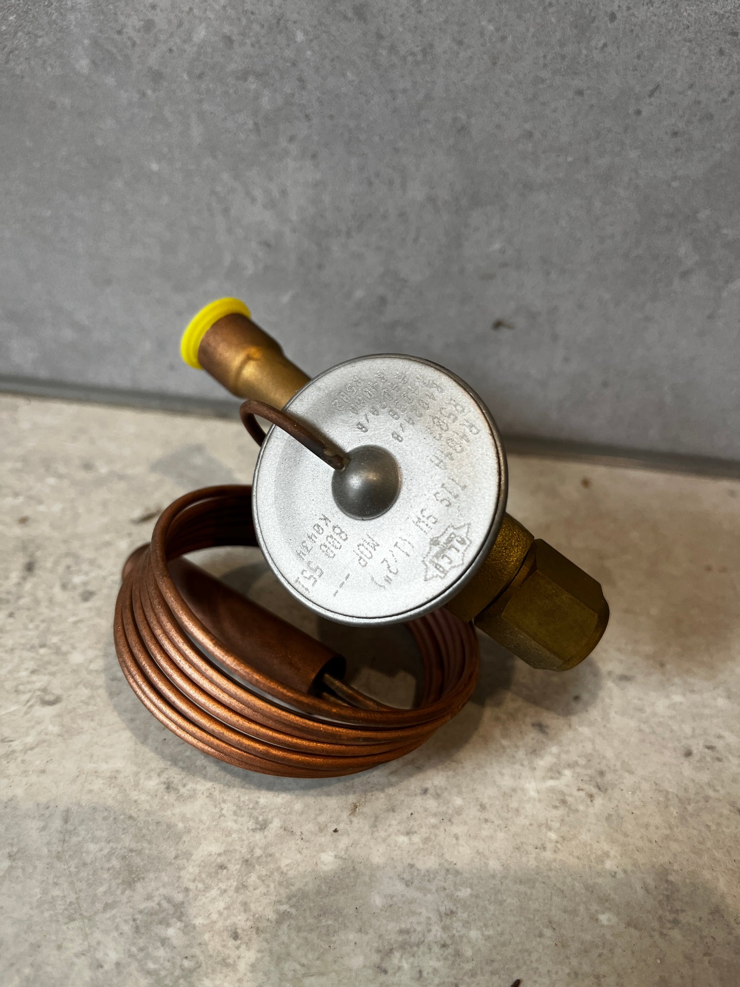 Top view of copper thermostatic expansion valve displaying coiled capillary tube and brass connector