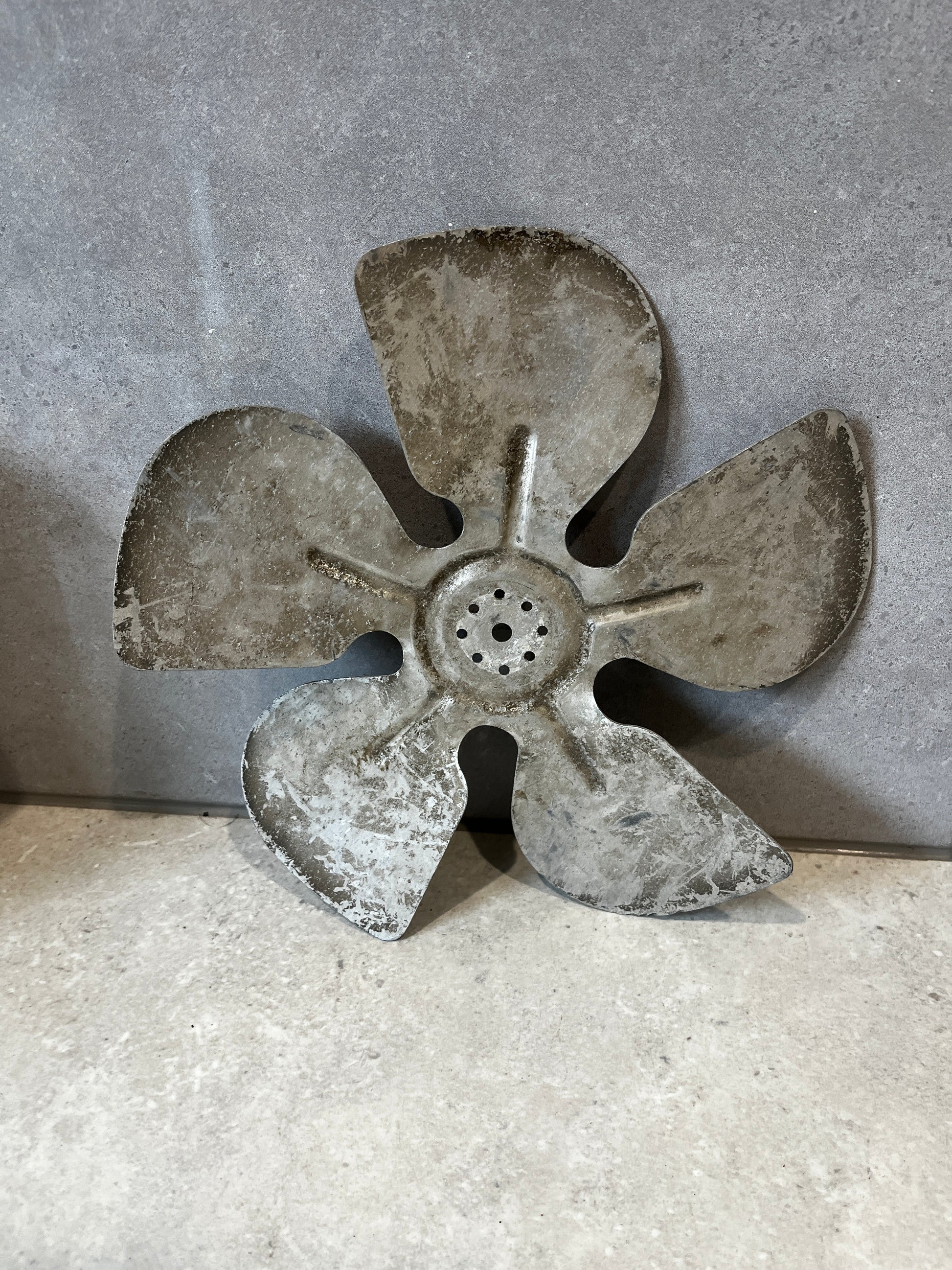 Full view of four-blade metal fan component on stone background