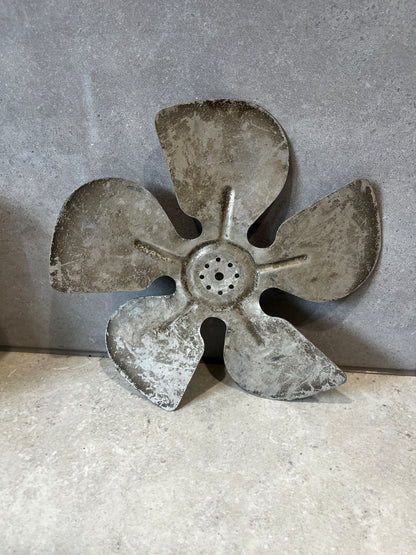 Full view of four-blade metal fan component on stone background