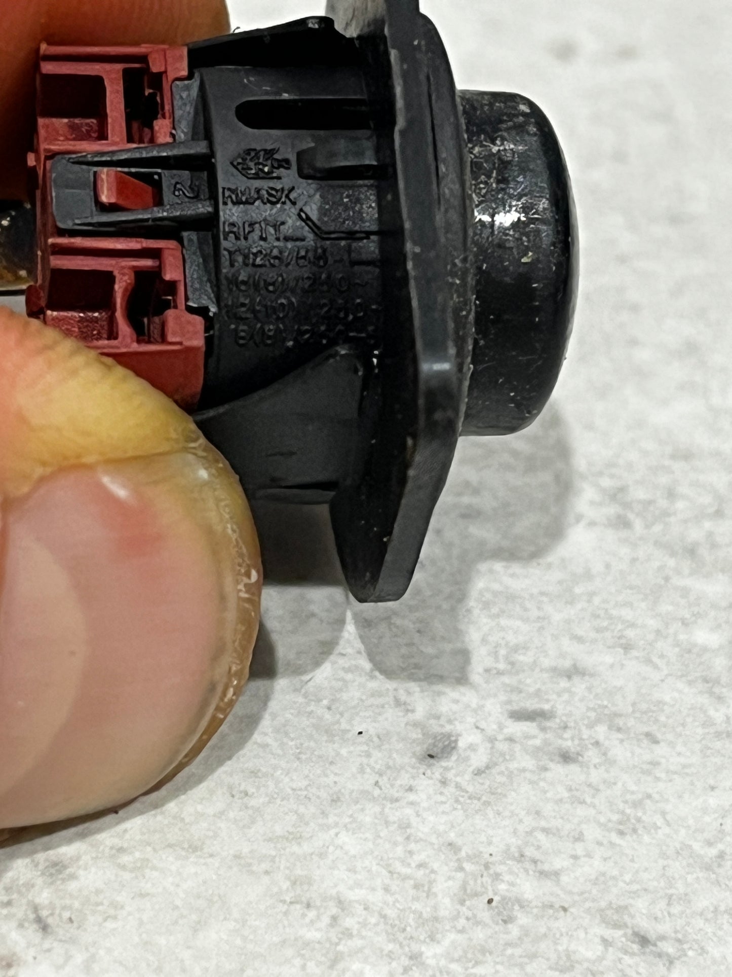 Close-up side view of black round rocker switch with manufacturing markings