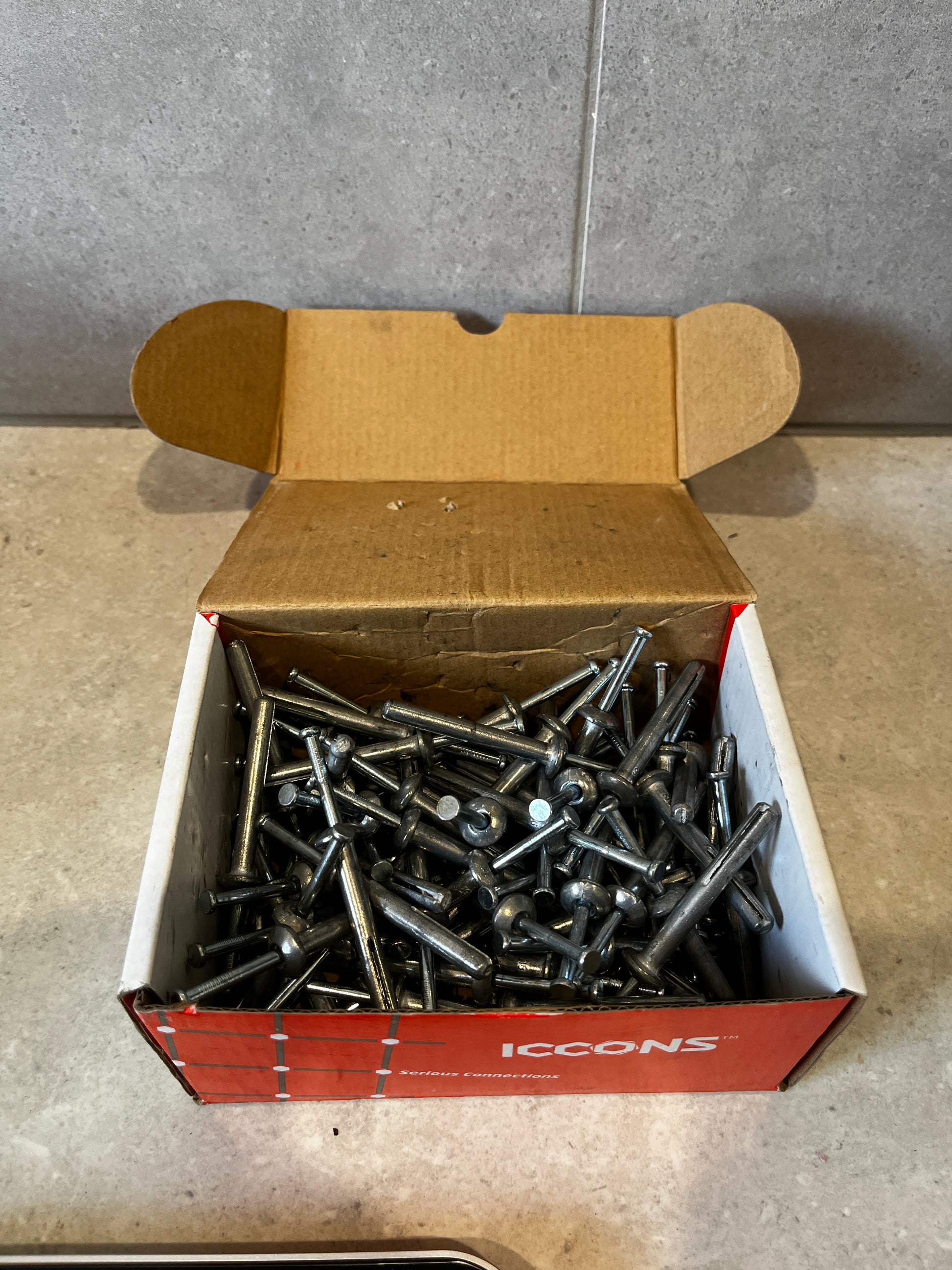 Open box of ICCONS metal drive anchors with several anchors visible
