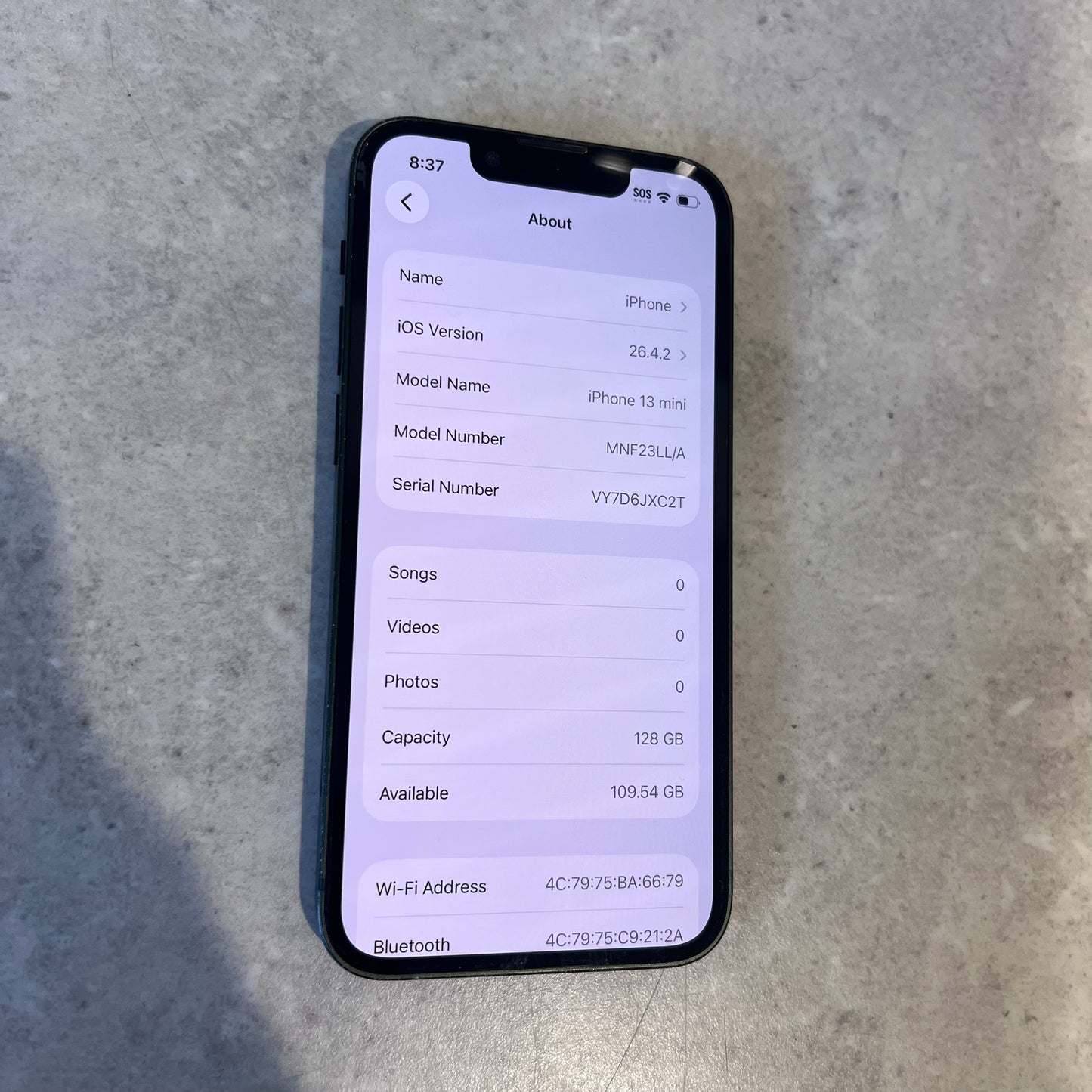 Screen close-up showing iPhone 13 Mini About page with 128GB capacity and iOS version 16.4.2