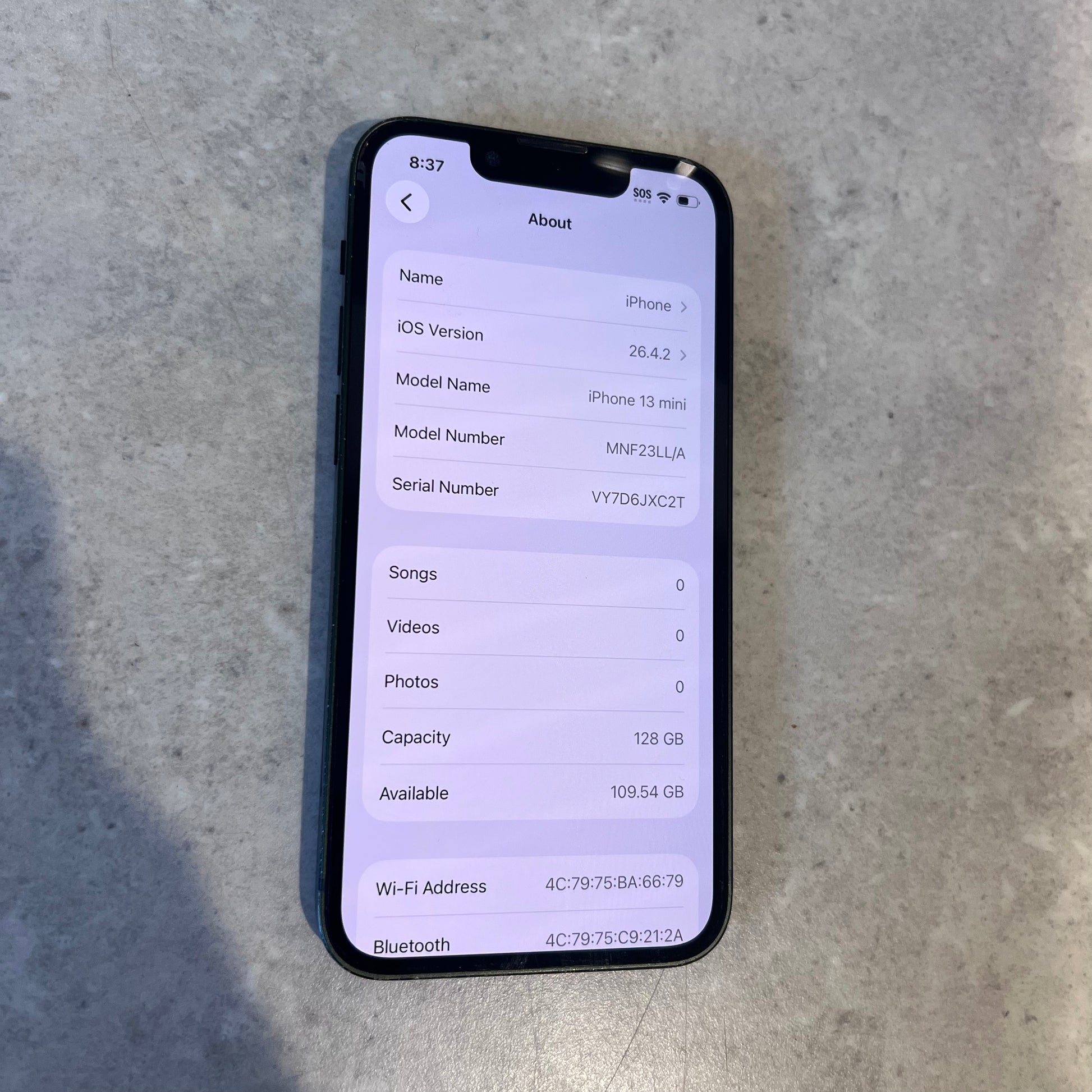 Screen close-up showing iPhone 13 Mini About page with 128GB capacity and iOS version 16.4.2