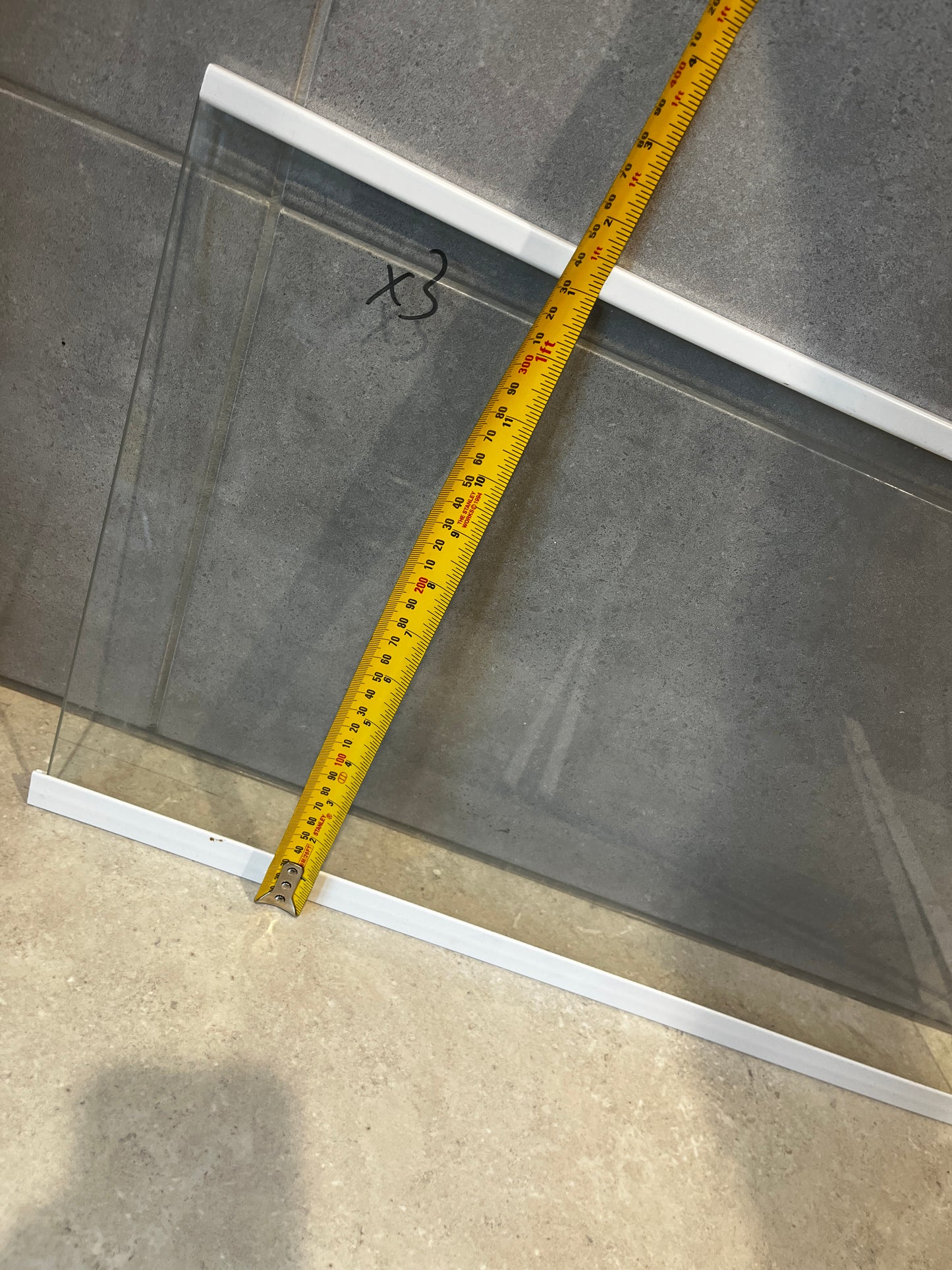 Close-up of clear glass panel with white frames measured vertically with yellow measuring tape