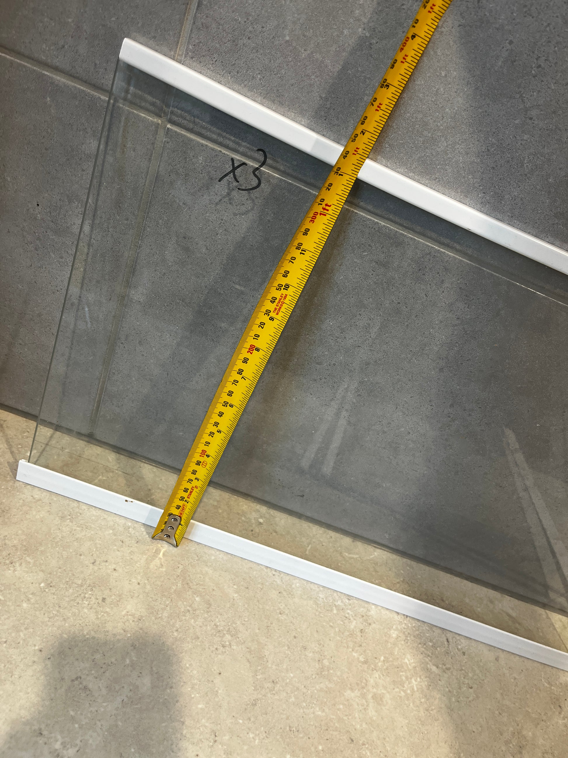 Close-up of clear glass panel with white frames measured vertically with yellow measuring tape