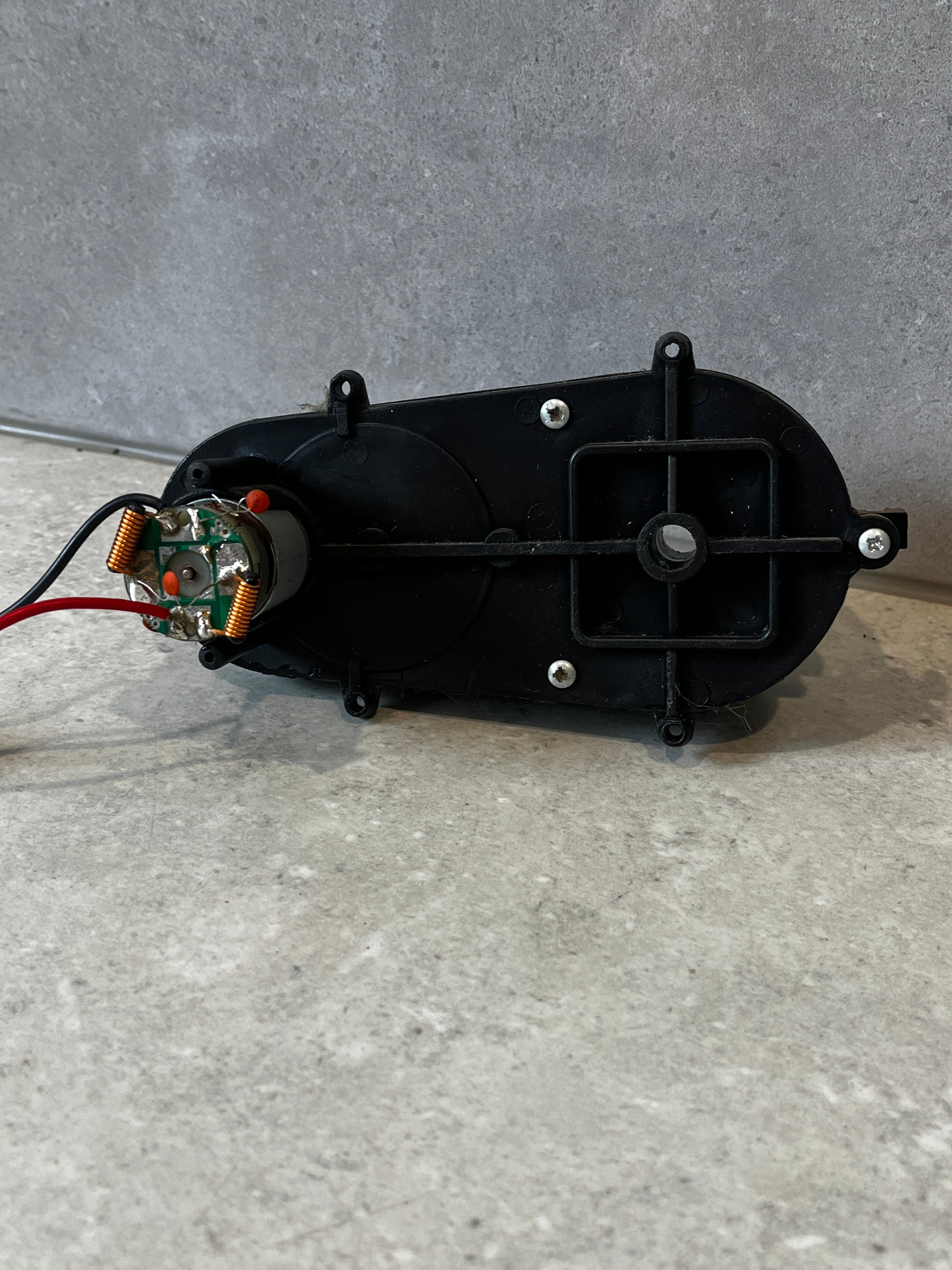 Rear view of black plastic gearbox housing with screws and wiring